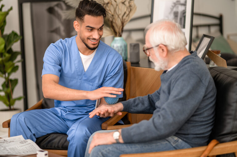 Smiling friendly physiatrist looking at an aged patient while massaging the back of his hand